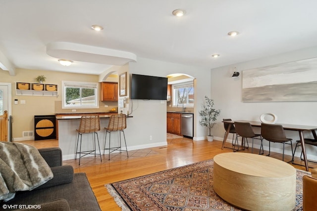 living room with light wood-style floors, arched walkways, a healthy amount of sunlight, and visible vents