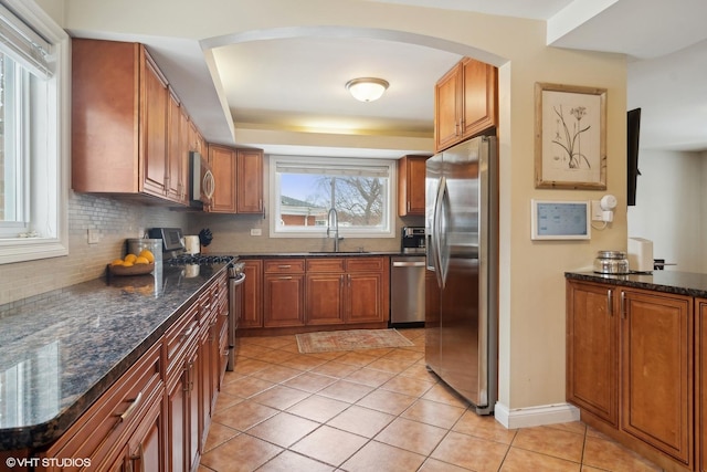 kitchen featuring brown cabinetry, arched walkways, tasteful backsplash, a sink, and appliances with stainless steel finishes