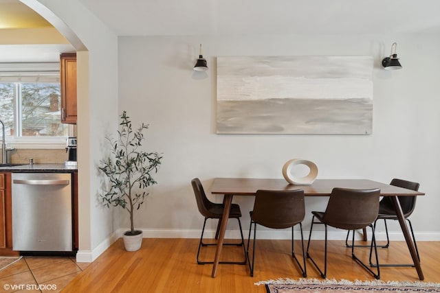 dining room with arched walkways, baseboards, and light wood finished floors