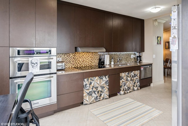 kitchen featuring light stone counters, appliances with stainless steel finishes, a sink, tasteful backsplash, and under cabinet range hood