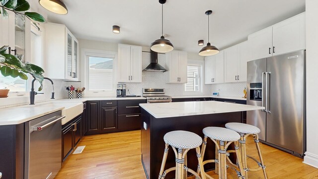 5650 W Grace St, Chicago, IL 60634 - kitchen featuring a breakfast bar area, a center island, white cabinets, stainless steel appliances, and wall chimney exhaust hood