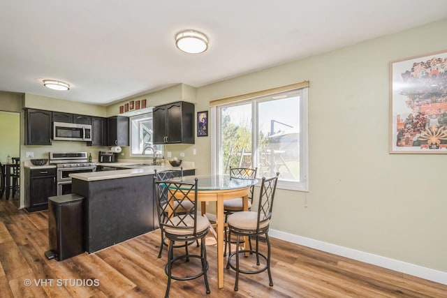 kitchen featuring appliances with stainless steel finishes, wood finished floors, light countertops, a sink, and baseboards