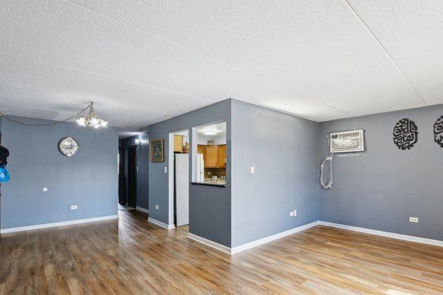 7310 Tiffany Dr Unit 2B, Orland Park, IL 60462 - unfurnished living room featuring a textured ceiling, baseboards, wood finished floors, and a notable chandelier