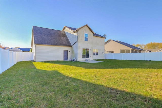 back of property with a lawn, a patio, roof with shingles, and a fenced backyard