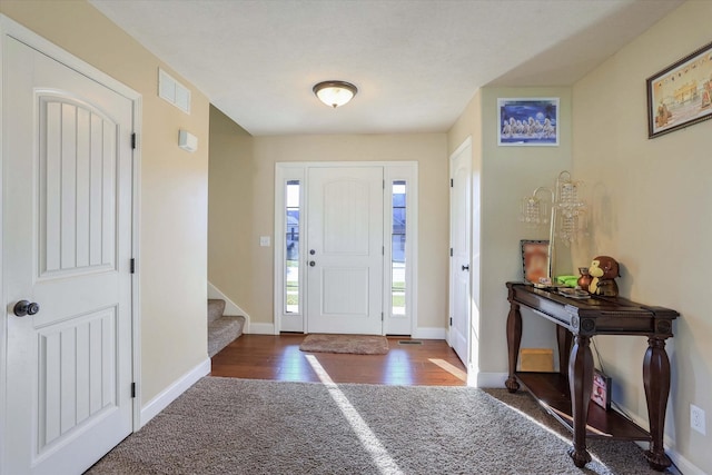 carpeted foyer featuring stairs, baseboards, visible vents, and wood finished floors