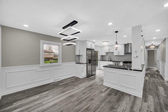 kitchen with stainless steel appliances, dark countertops, dark wood-style floors, a sink, and wall chimney exhaust hood