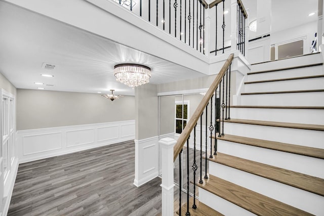 staircase featuring a chandelier, wood finished floors, wainscoting, a decorative wall, and recessed lighting