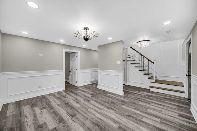 unfurnished living room with a chandelier, stairs, a decorative wall, wood finished floors, and recessed lighting