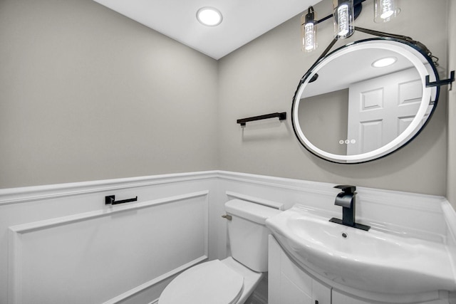 bathroom with a wainscoted wall, toilet, vanity, and a decorative wall