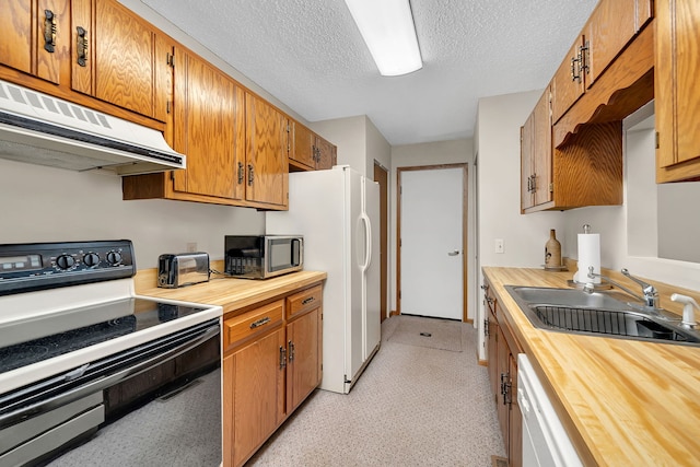kitchen with white appliances, under cabinet range hood, butcher block counters, and a sink