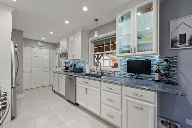 kitchen with glass insert cabinets, white cabinetry, tasteful backsplash, a sink, and stainless steel appliances