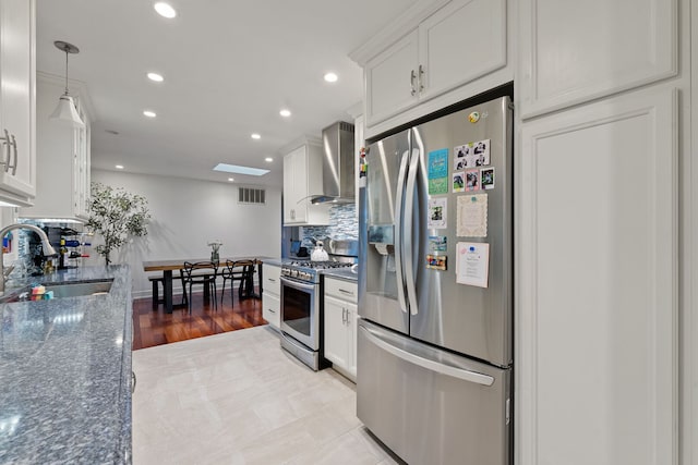 kitchen with white cabinets, stainless steel appliances, a sink, and wall chimney exhaust hood