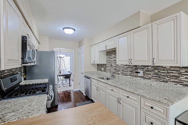 kitchen with appliances with stainless steel finishes, tasteful backsplash, a sink, dark wood-style floors, and a notable chandelier