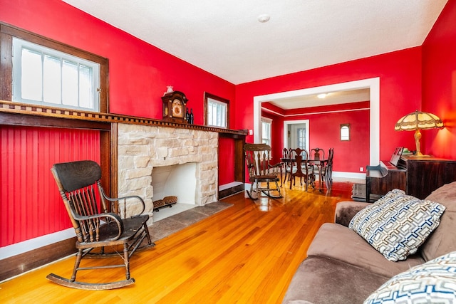 living area with wood-type flooring, baseboards, and a stone fireplace