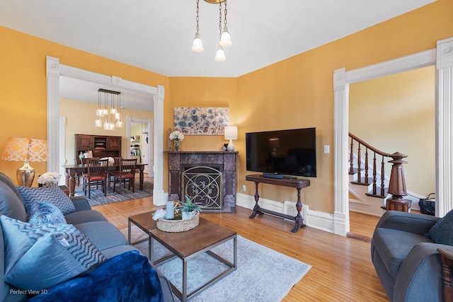 living area featuring wood finished floors, ornate columns, stairway, a fireplace, and baseboards