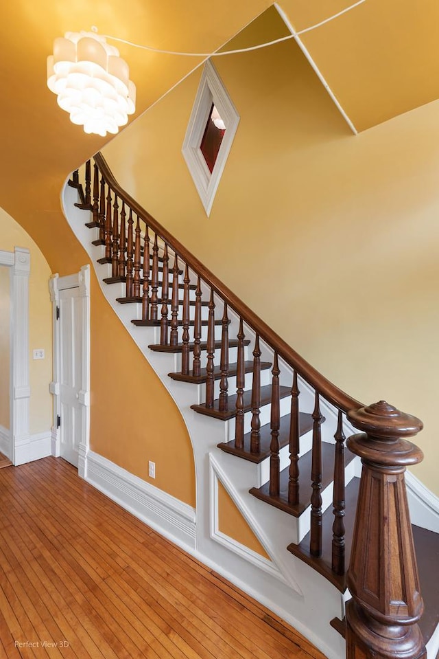 staircase featuring baseboards, an inviting chandelier, and wood-type flooring