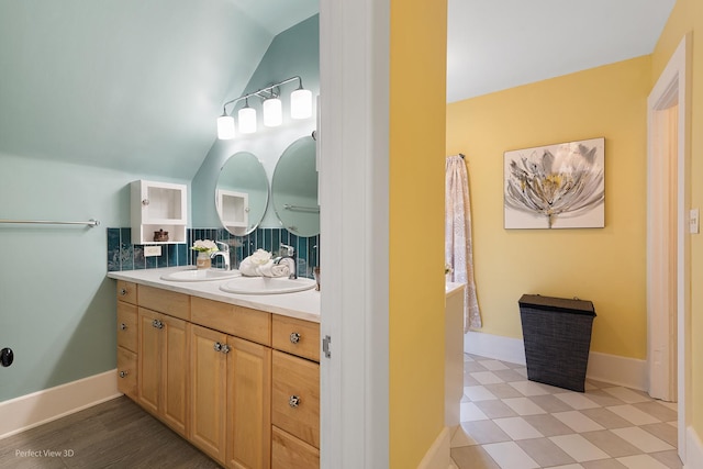 bathroom featuring vanity, baseboards, tasteful backsplash, and vaulted ceiling