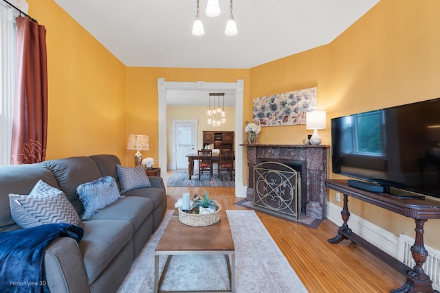 living room featuring a chandelier, baseboards, a fireplace with flush hearth, and wood finished floors