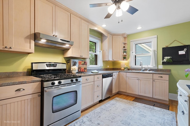 kitchen with a sink, under cabinet range hood, light wood-style flooring, a ceiling fan, and appliances with stainless steel finishes