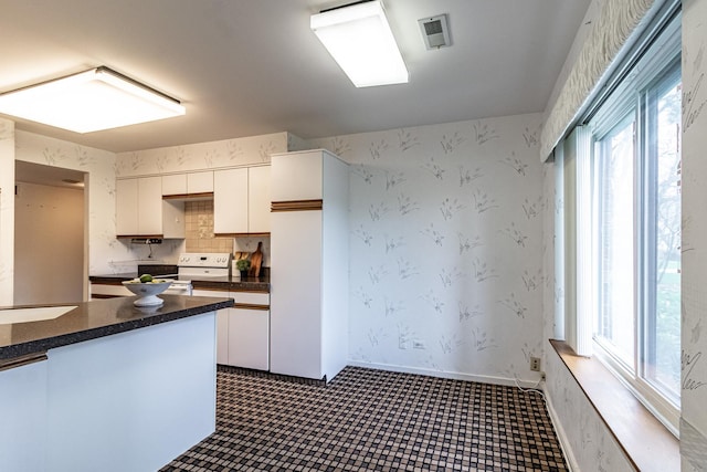 kitchen with white cabinets, electric range, dark countertops, wallpapered walls, and visible vents