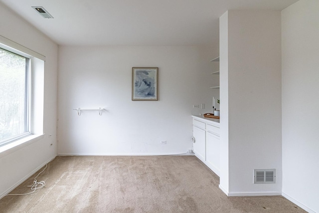 spare room with a healthy amount of sunlight, light carpet, and visible vents