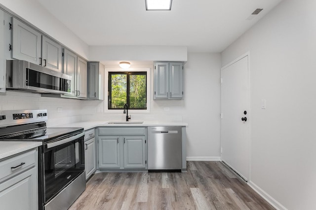 kitchen with stainless steel appliances, a sink, gray cabinets, light countertops, and light wood-style flooring