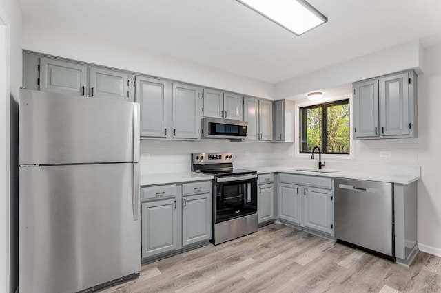 kitchen featuring stainless steel appliances, gray cabinets, a sink, and backsplash