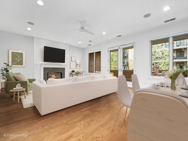 living area with light wood finished floors, a glass covered fireplace, ceiling fan, and recessed lighting
