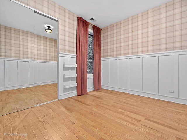 spare room with wallpapered walls, a decorative wall, wood finished floors, and a wainscoted wall