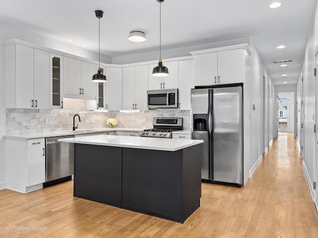 kitchen featuring stainless steel appliances, a sink, light countertops, a center island, and glass insert cabinets