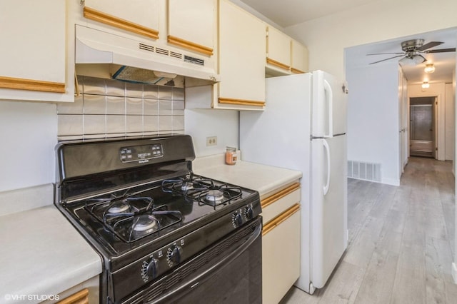 kitchen with black gas range, under cabinet range hood, light countertops, tasteful backsplash, and light wood finished floors