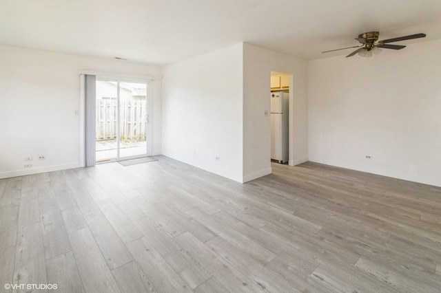 spare room featuring light wood-type flooring, a ceiling fan, and baseboards