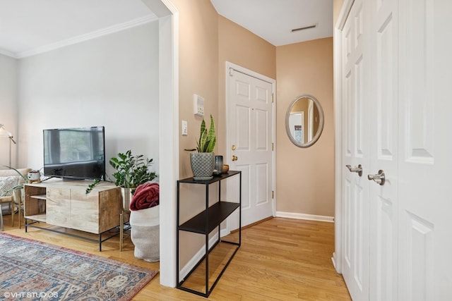 foyer featuring crown molding, baseboards, light wood-type flooring, and visible vents
