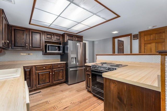 kitchen featuring a sink, stainless steel appliances, butcher block counters, dark brown cabinetry, and light wood finished floors