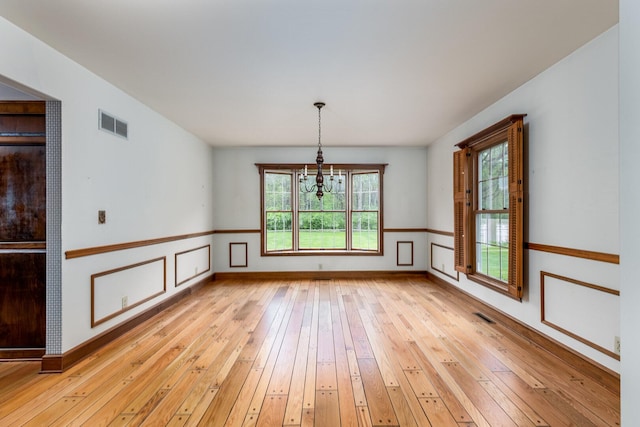 unfurnished dining area featuring an inviting chandelier, plenty of natural light, light wood-type flooring, and visible vents