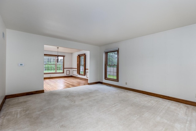 empty room featuring a chandelier, carpet flooring, baseboards, and visible vents