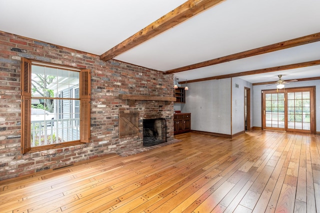 unfurnished living room with a brick fireplace, wood-type flooring, beam ceiling, and plenty of natural light