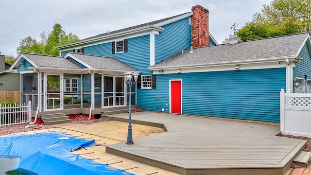 rear view of house featuring a chimney, fence, a sunroom, a deck, and roof with shingles
