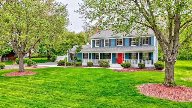 colonial-style house with a porch, roof with shingles, and a front lawn