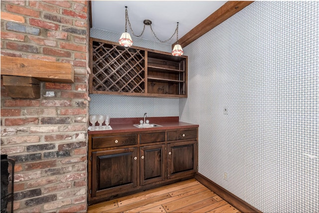bar with wallpapered walls, baseboards, light wood finished floors, a sink, and indoor wet bar