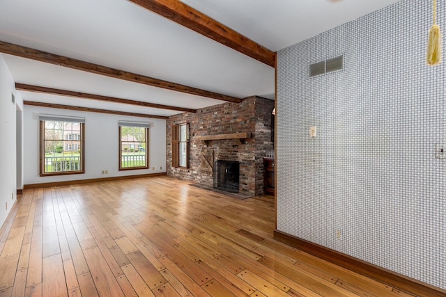 unfurnished living room featuring a fireplace, beam ceiling, baseboards, and light wood-style floors