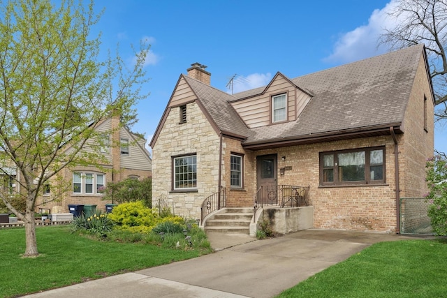 view of front of house featuring stone siding, a chimney, a shingled roof, a front yard, and brick siding