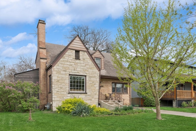 rear view of property featuring a chimney, stone siding, and a lawn