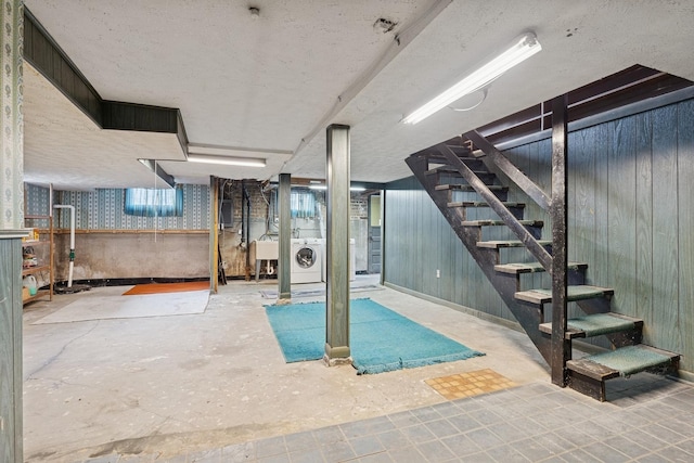below grade area with a sink, a textured ceiling, wood walls, washer / clothes dryer, and stairs