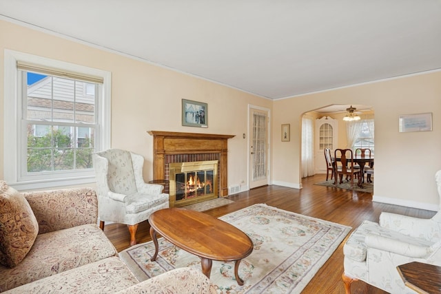 living area with baseboards, ornamental molding, a fireplace with flush hearth, wood finished floors, and arched walkways