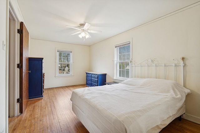 bedroom with light wood finished floors, multiple windows, baseboards, and a ceiling fan