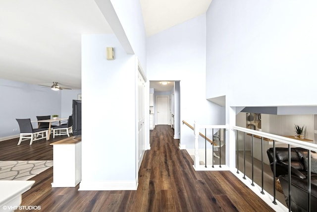 corridor featuring baseboards, a towering ceiling, wood finished floors, and an upstairs landing