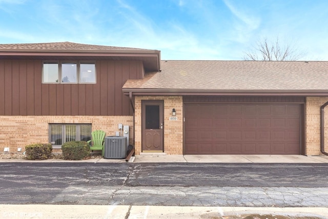 tri-level home with brick siding, an attached garage, driveway, and central AC unit