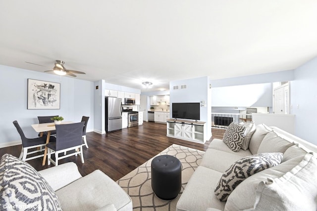 living room with a ceiling fan, baseboards, visible vents, and dark wood-type flooring