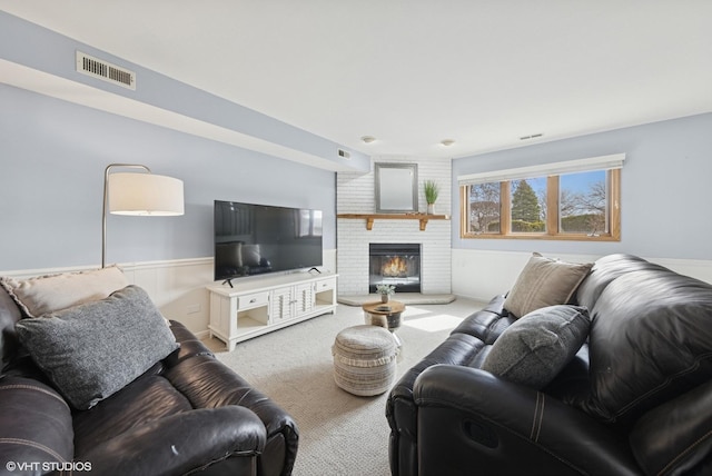 living area featuring carpet flooring, visible vents, wainscoting, and a brick fireplace